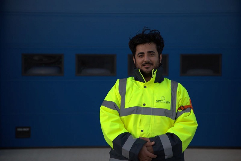 A smiling Octagon Risk Management security guard in a yellow hi-vis jacket